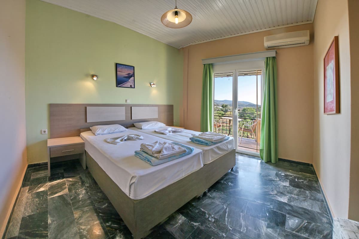 A double bed with a headboard, a nightstand, and a window with a view of the outdoors.