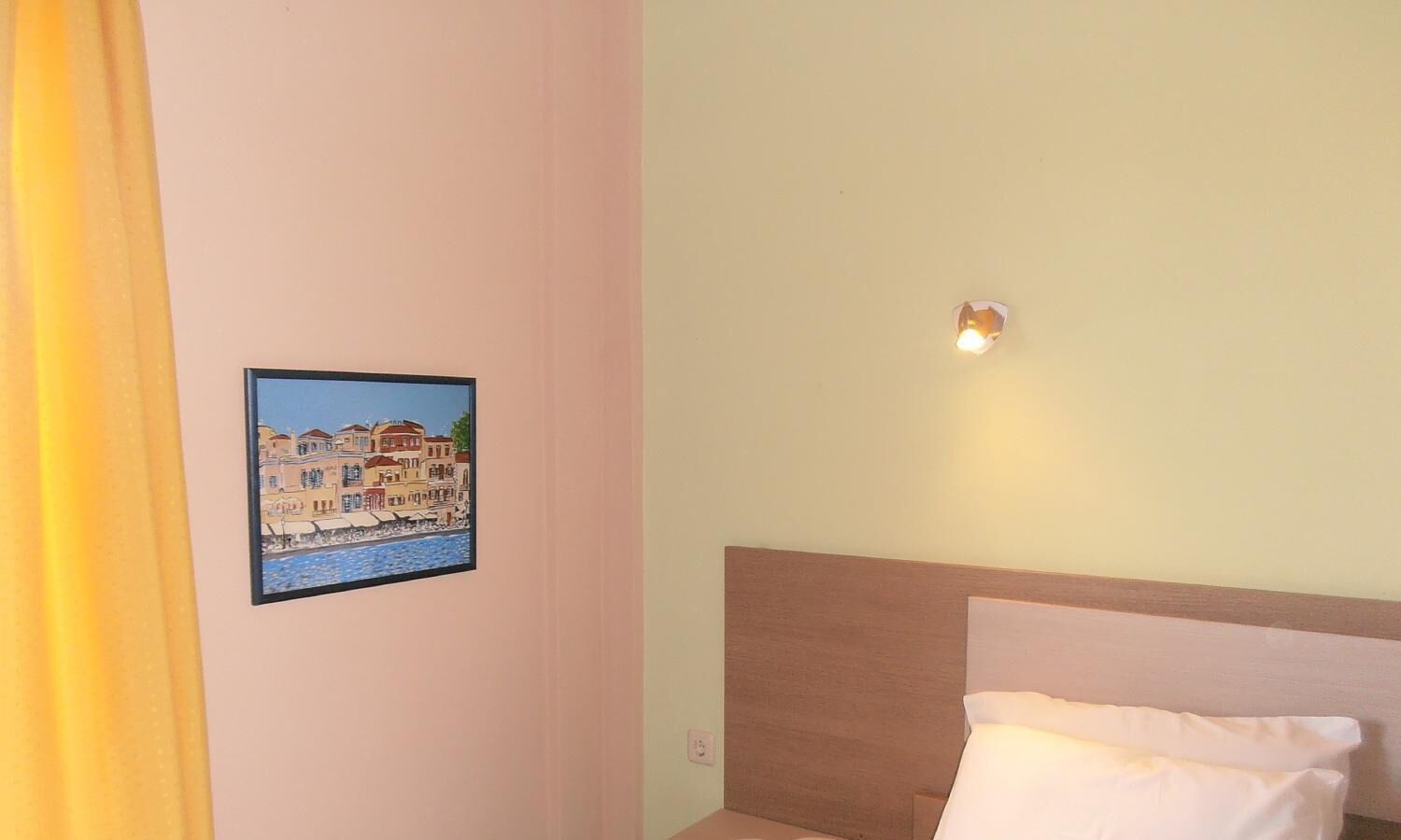 A bedroom with a bed, a headboard, a wall-mounted light, and a framed picture of a building.