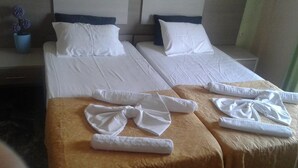 A hotel room with two beds, each with white linens and pillows. There are towels neatly arranged on a wooden table in front of each bed. - Armonia Studios (Lesvos)