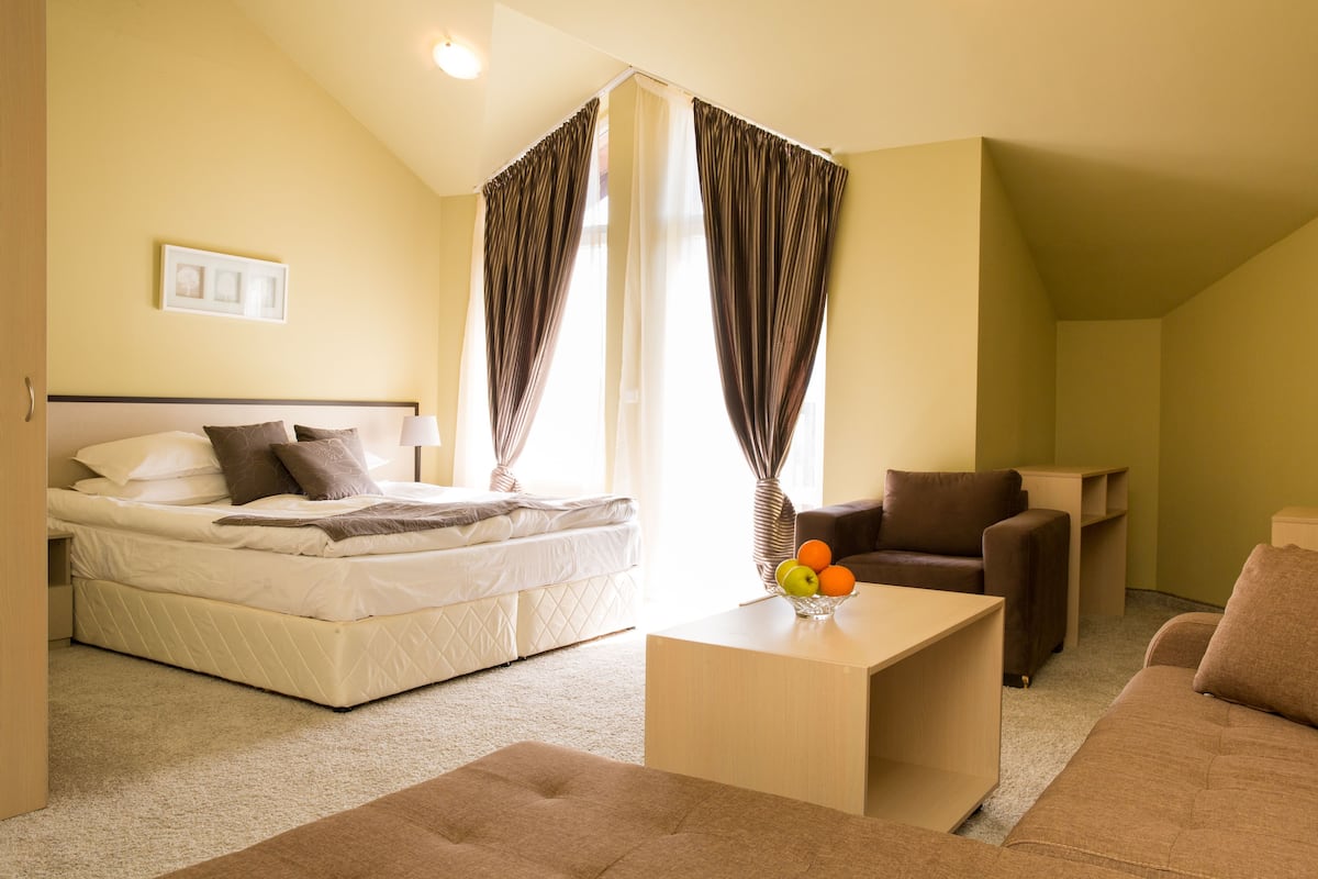 A bedroom with a bed, a sofa, a coffee table, and curtains.
