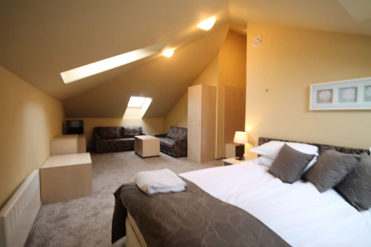 A hotel room with a bed, a sofa, a small table, and a lamp.