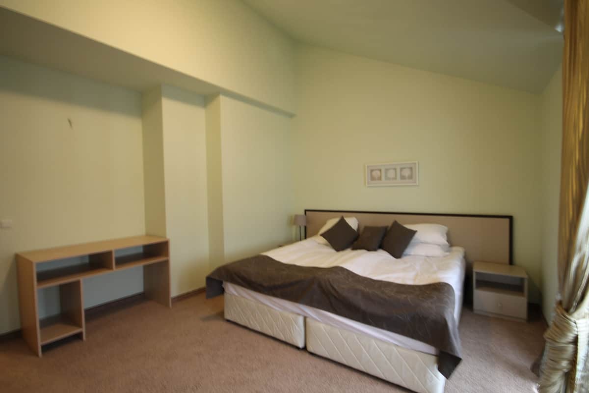 A bedroom with a bed, bedside tables, a bench, and a wall-mounted shelf.