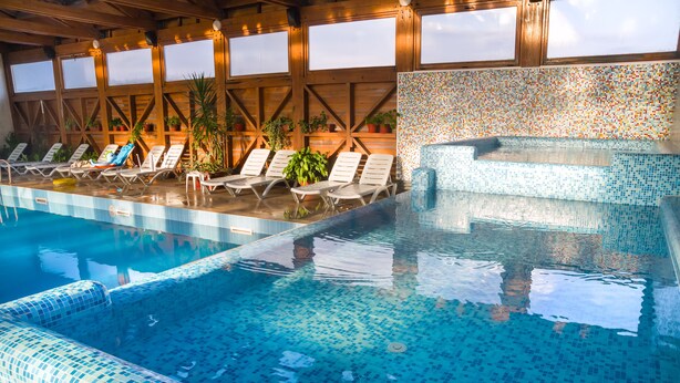 Una piscina con paredes de azulejos y techo de madera, rodeada de sillas de descanso y plantas en macetas.