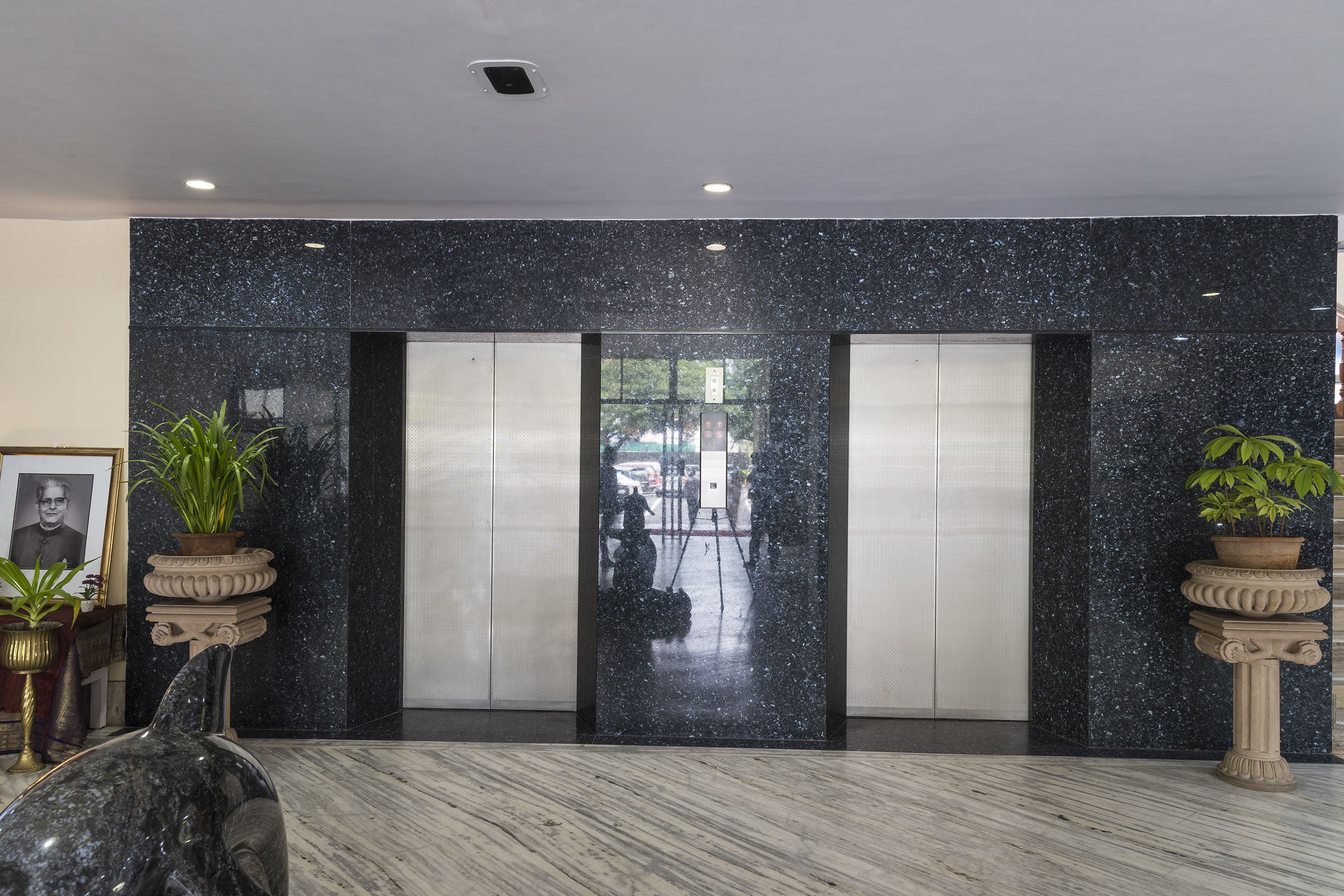 A lobby with marble flooring, two elevators, and potted plants.