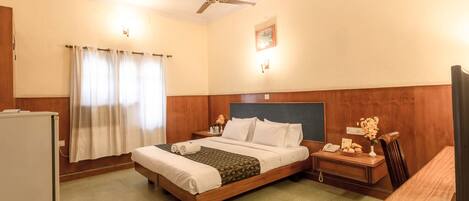 A hotel room with a bed, bedside tables, a desk, a chair, a ceiling fan, and a window with curtains.