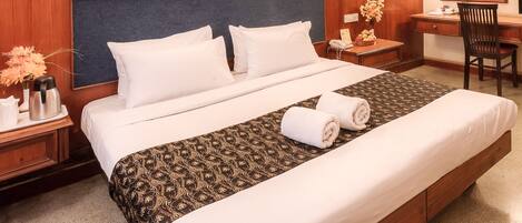 A hotel room with a large bed, wooden headboard, bedside tables with lamps, a desk, and a chair.