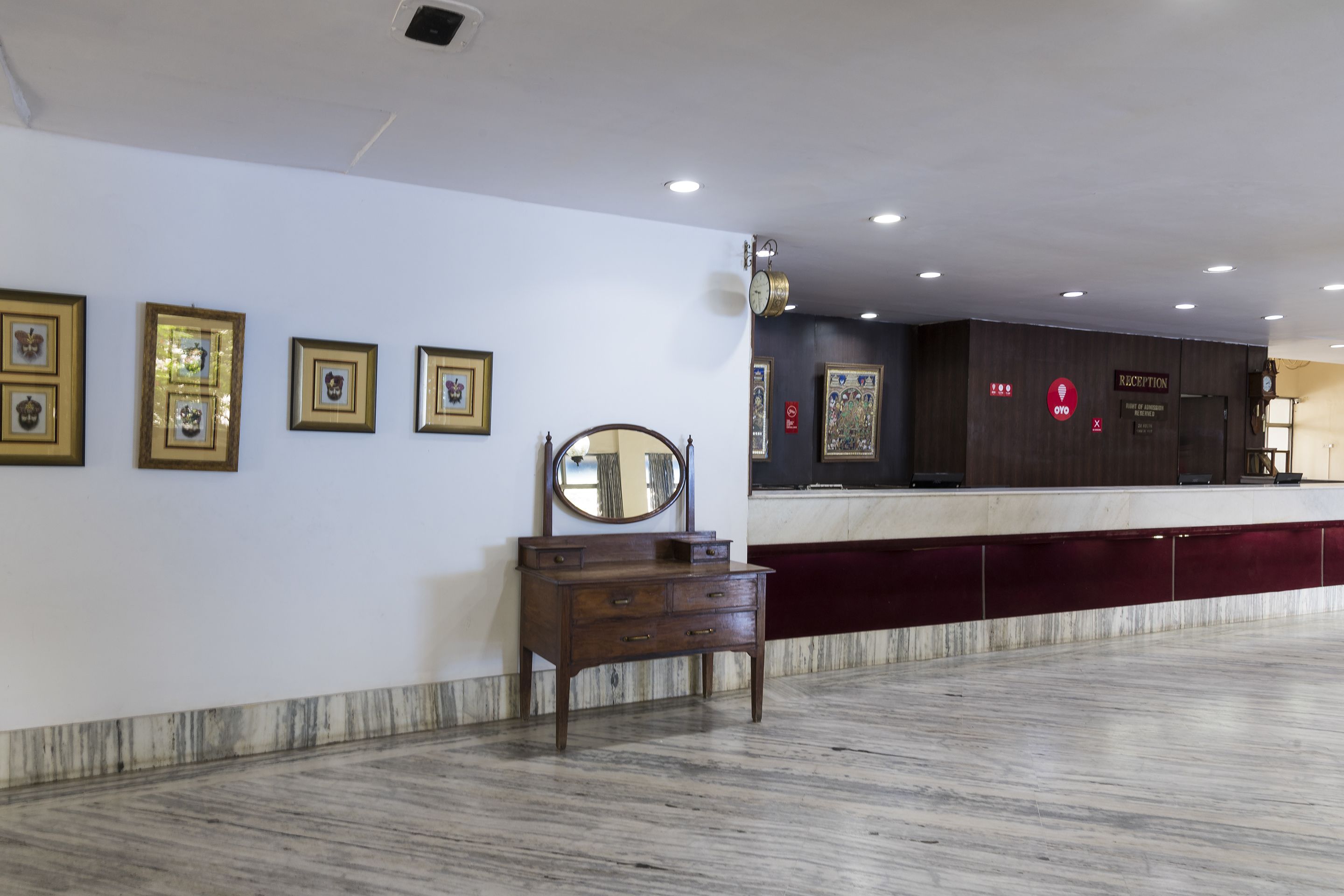 Uma área de recepção com piso de mármore, cômoda de madeira e quadros nas paredes.