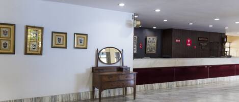 Uma área de recepção com piso de mármore, cômoda de madeira e quadros nas paredes.