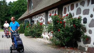 Un bâtiment en pierre avec un toit de chaume, un chemin pavé et des rosiers rouges dans le jardin.