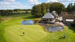 Ein Golfplatz mit Teich, Clubhaus und Steinhaus.
