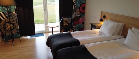 Habitación de hotel con una cama grande, una silla, una mesita y vistas a un espacio verde a través de un ventanal.
