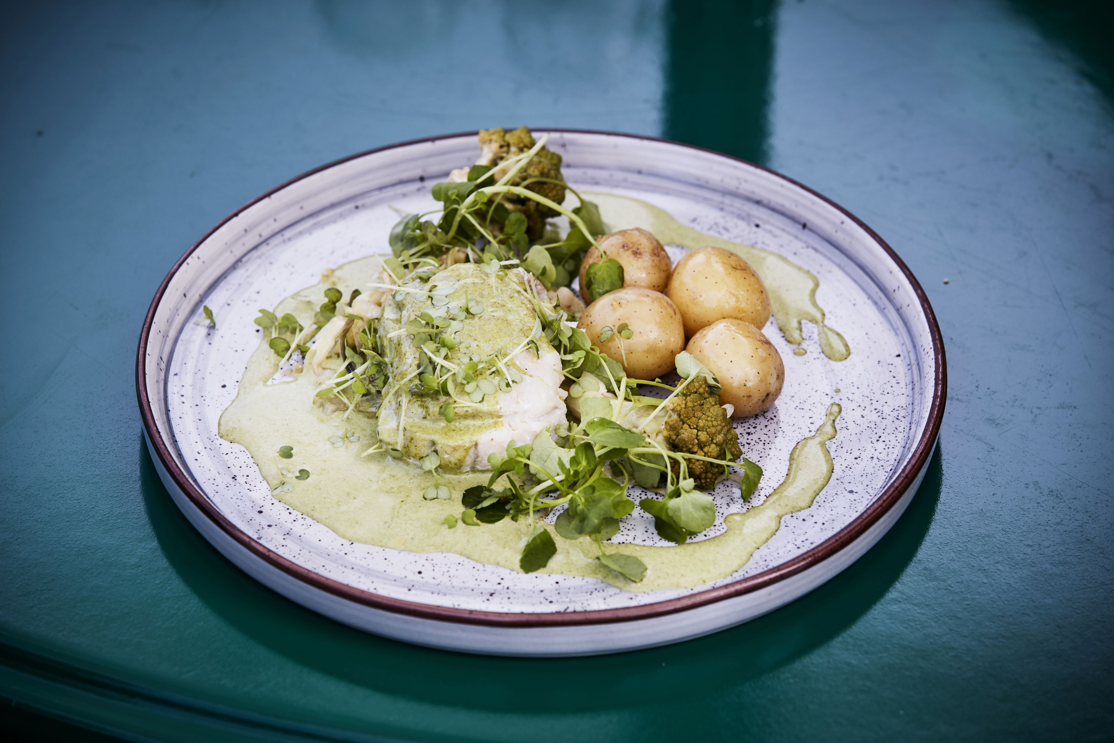 A plate of food with greens, potatoes, and a creamy sauce on a ceramic plate.