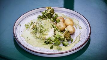 A plate of food with greens, potatoes, and a creamy sauce on a ceramic plate.