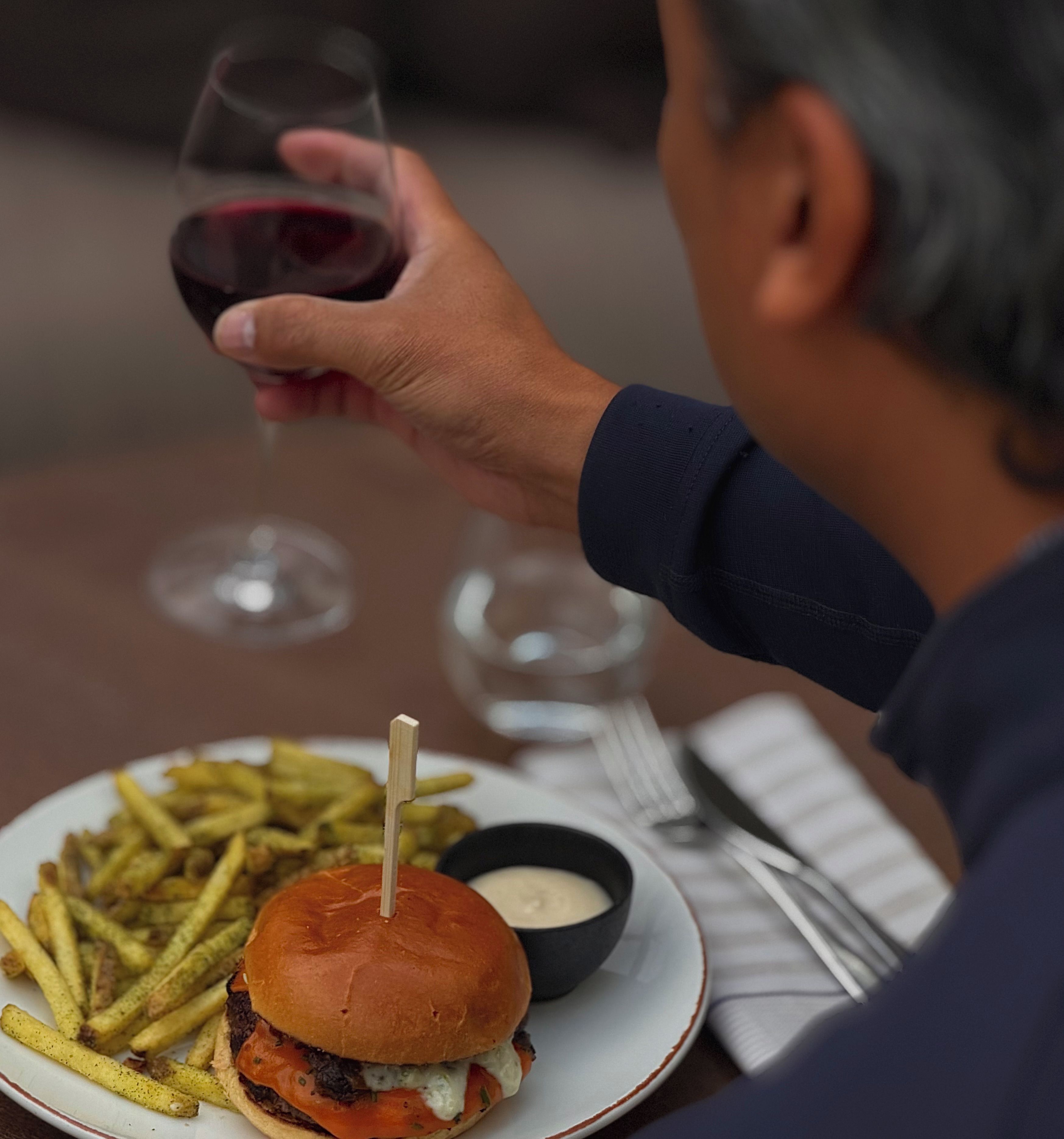 A person dining with a burger, fries, and a drink on a table.