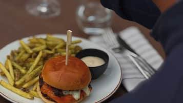 A person dining with a burger, fries, and a drink on a table.
