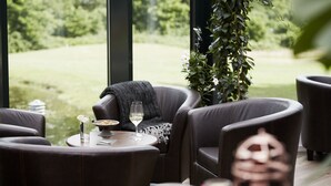 Ein Essbereich mit Ledersesseln, einem runden Tisch und Blick auf einen Golfplatz durch große Fenster.
