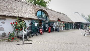 Una tienda con techo de paja, un letrero que dice "Shop-Reception" y bicicletas estacionadas afuera.