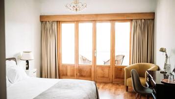 Una habitación de hotel con una cama grande, un escritorio, una silla y vistas a través de un ventanal corredero.