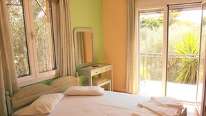 A bedroom with a bed, a bedside table, a mirror, and a view of the outdoors. - Kipos Studios (Lesvos)