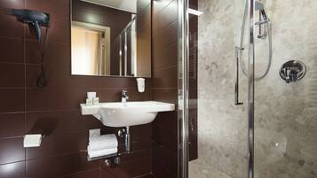 Ein modernes Badezimmer mit Duschabtrennung aus Glas, einem weißen Waschbecken und einem an der Wand befestigten Föhn.
