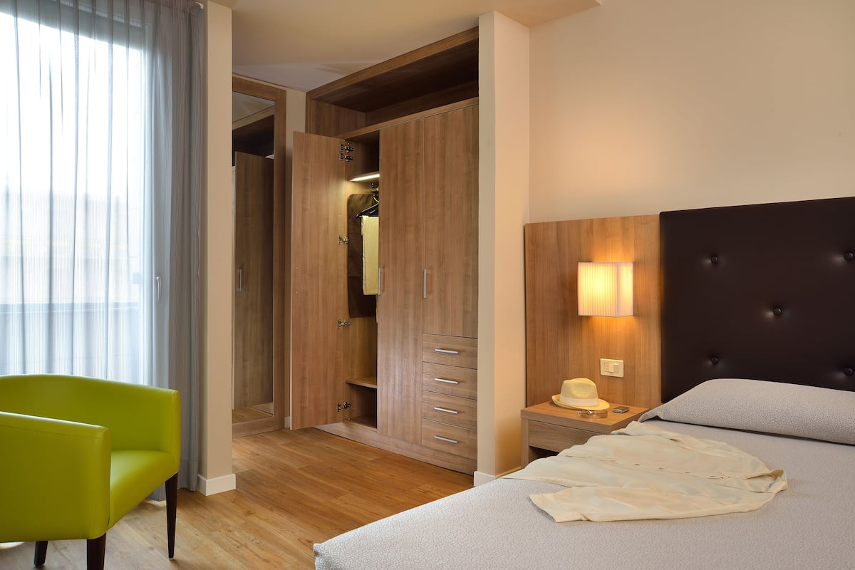 Una habitación de hotel con una cama, una mesita de noche, una lámpara, un armario y una silla.