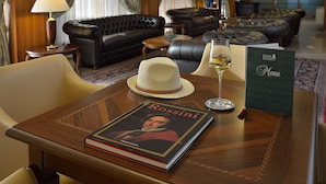 Ein Hotelzimmer mit einer Ledersofa, einem Esstisch mit einem Buch mit dem Titel 'Rossini', einem Weinglas und einem Menüständer.