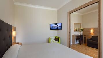 A hotel room with a bed, a TV mounted on the wall, a desk with a chair, and a mirror.