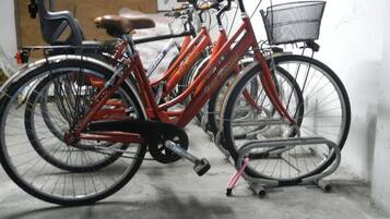 A bicycle with a basket and a kickstand in a room with a concrete floor and a chair in the background.