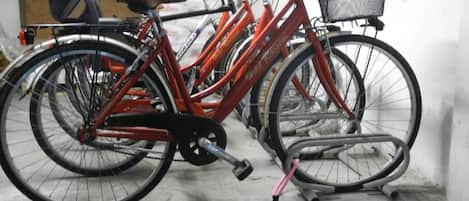 A bicycle with a basket and a kickstand in a room with a concrete floor and a chair in the background.