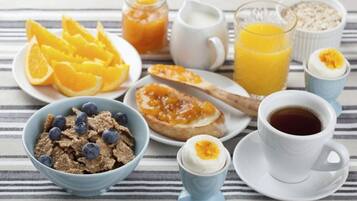 Mesa de café da manhã com cereal, frutas, torrada com geleia, café e suco sobre uma toalha xadrez.