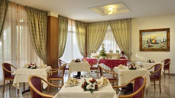 Un comedor con mesas dispuestas para cuatro comensales, cada una con mantel blanco, sillas rojas y centros de mesa con flores.
