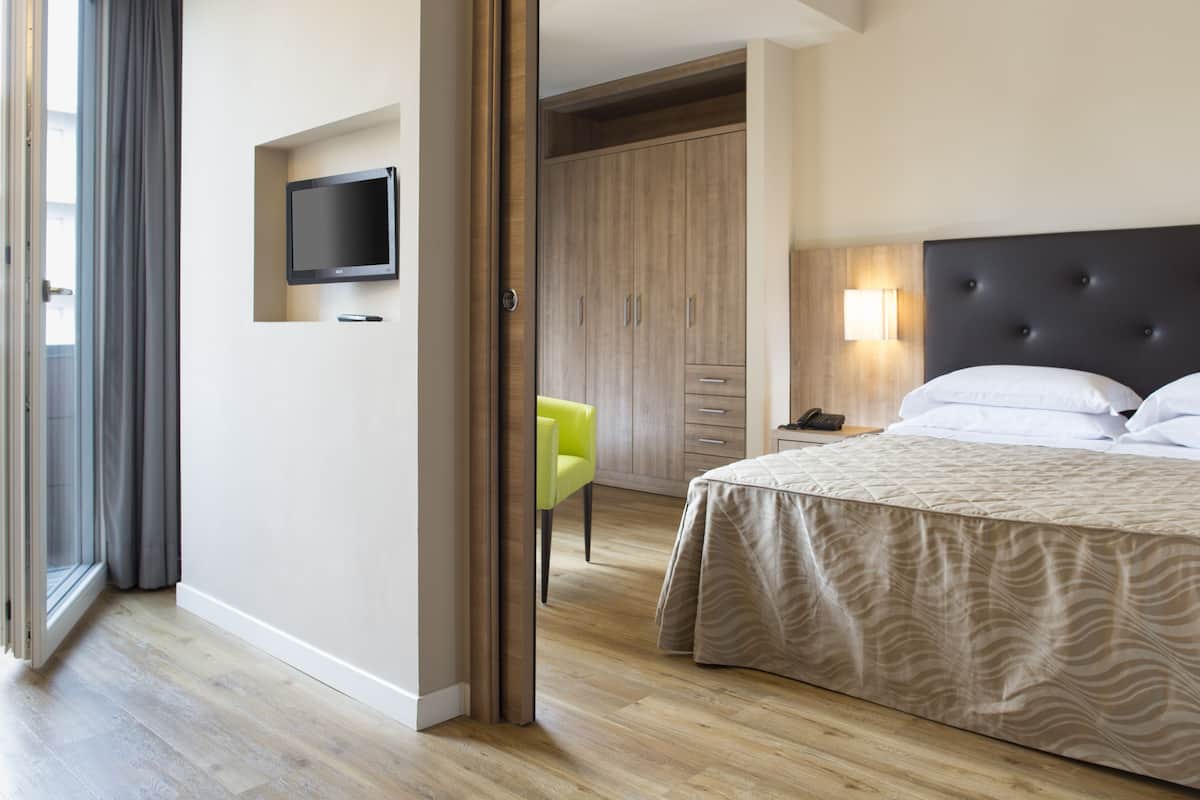 Una habitación de hotel con cama, escritorio, silla, armario y televisor en la pared.
