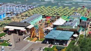 Ein Küstenbereich mit zahlreichen Sonnenschirmen, einem Spielplatz und einem Restaurant namens "SAMPLEI".