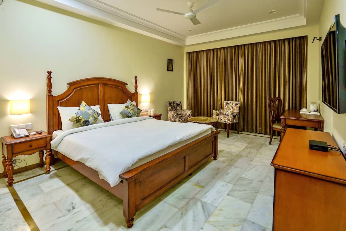 A hotel room with a large bed, a desk, a chair, a television, and a ceiling fan.