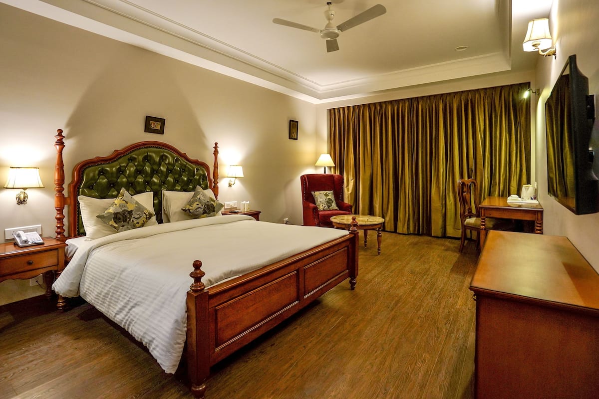 A hotel room with a large bed, a desk, a chair, a round table, and a ceiling fan.