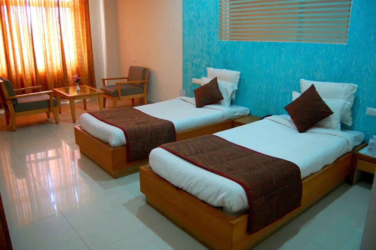 A hotel room with two beds, a small table, a chair, and a window with blinds.