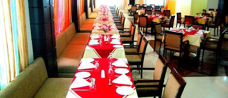 A restaurant with long tables set for dining, booths along the walls, and a bright interior.