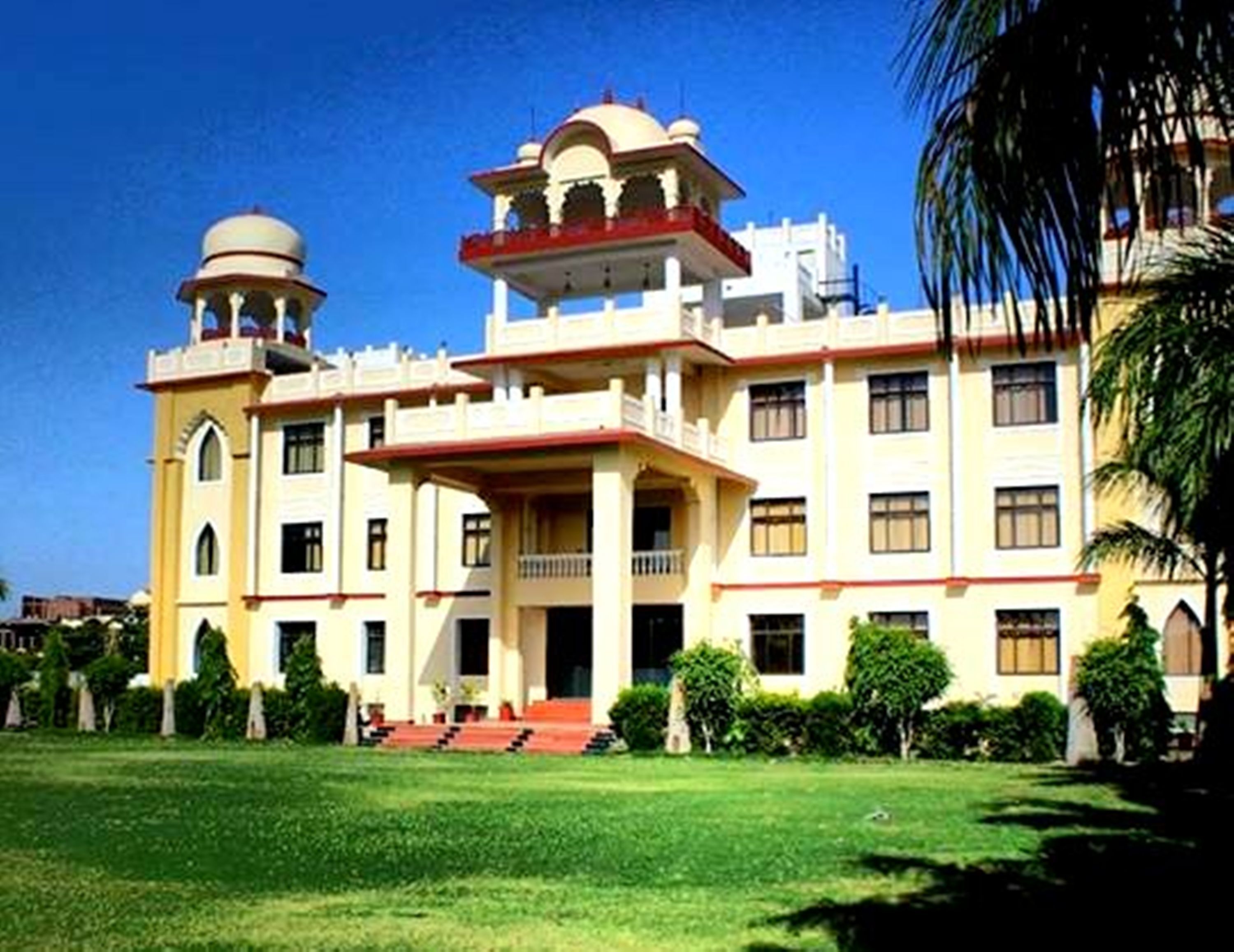 A large, multi-story building with a central courtyard, featuring a prominent dome and a balcony with a red railing.