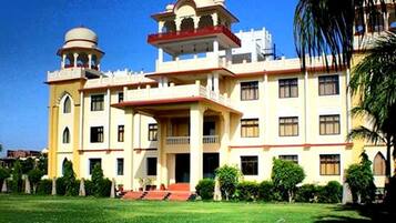 A large, multi-story building with a central courtyard, featuring a prominent dome and a balcony with a red railing.