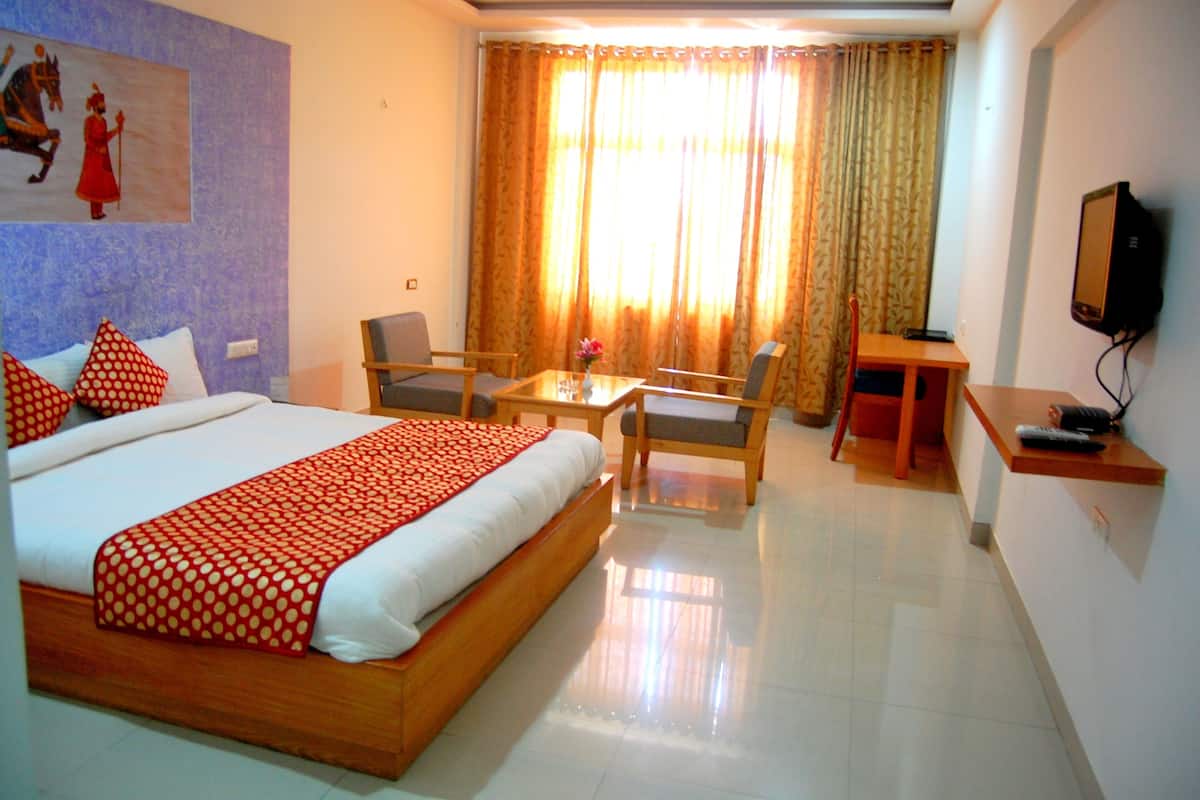 A hotel room with a large bed, a desk with a chair, a television, and a window with curtains.