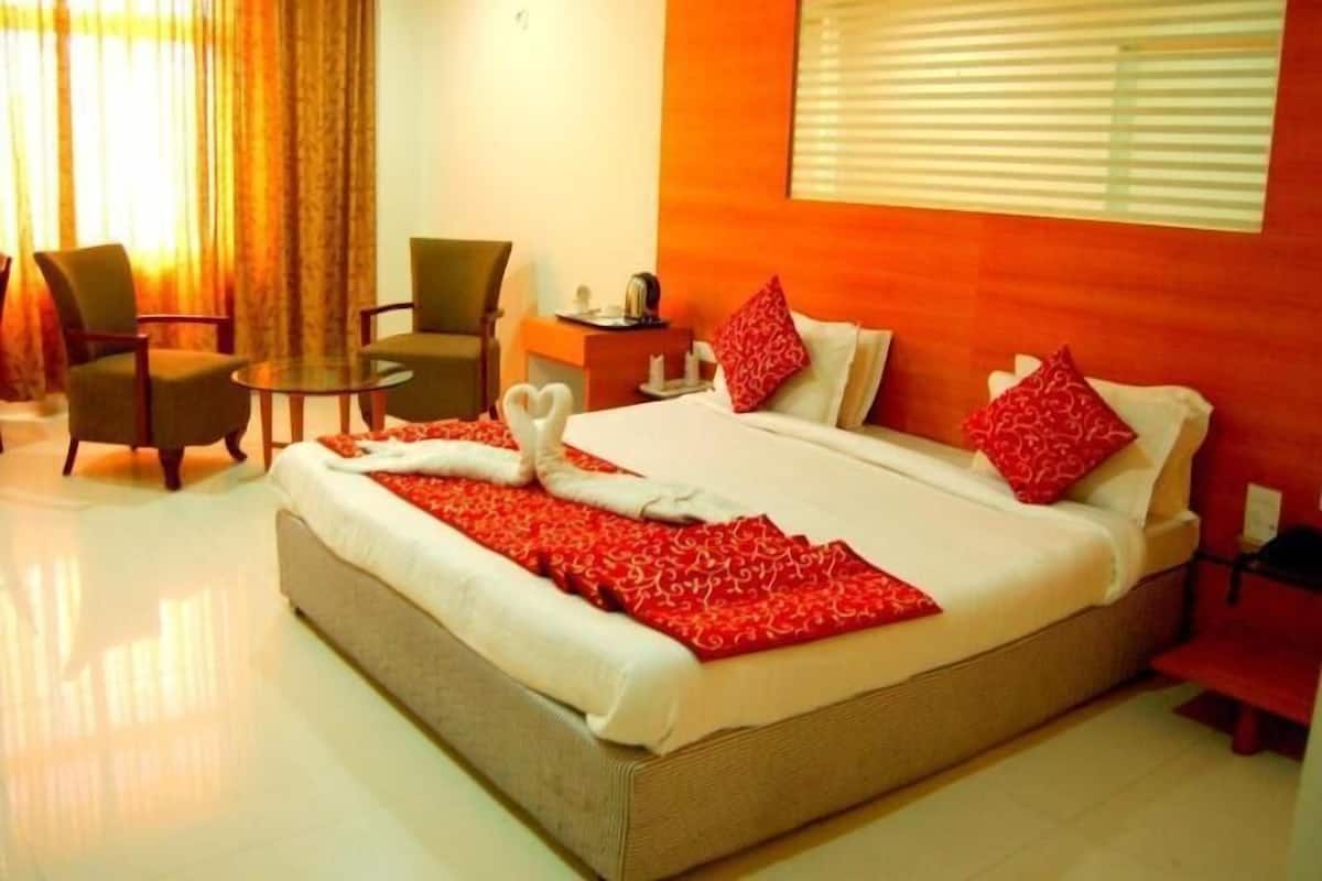 A hotel room with a large bed, a desk, a chair, and a window with blinds.