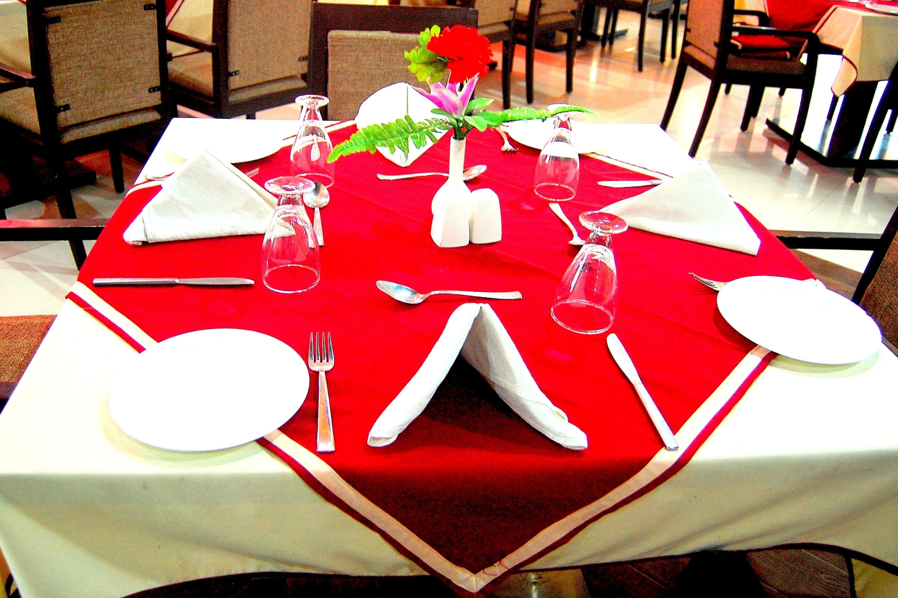 Une table à manger dressée avec de la vaisselle blanche et une nappe rouge.