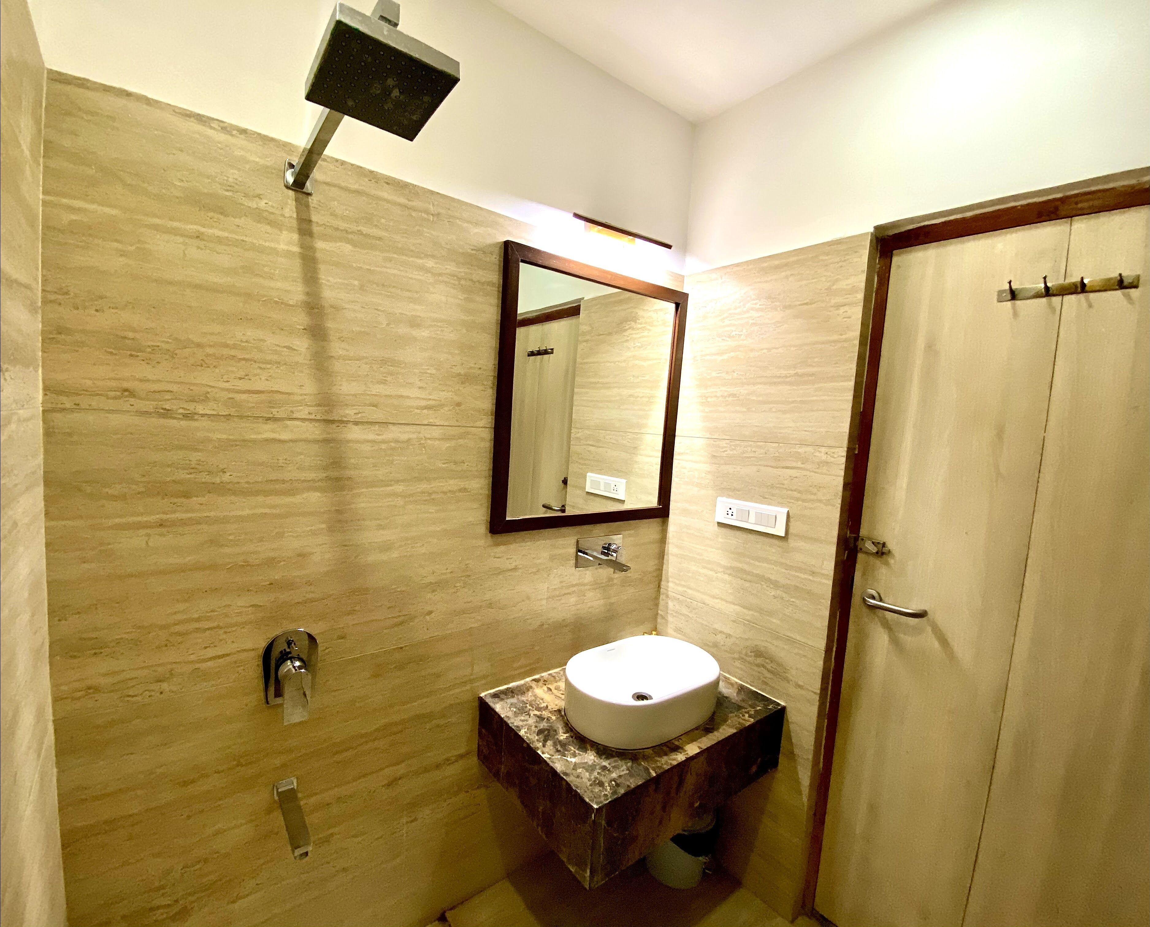 A bathroom with a marble vanity, a sink, a mirror, a showerhead, and a door.