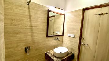 A bathroom with a marble vanity, a sink, a mirror, a showerhead, and a door.
