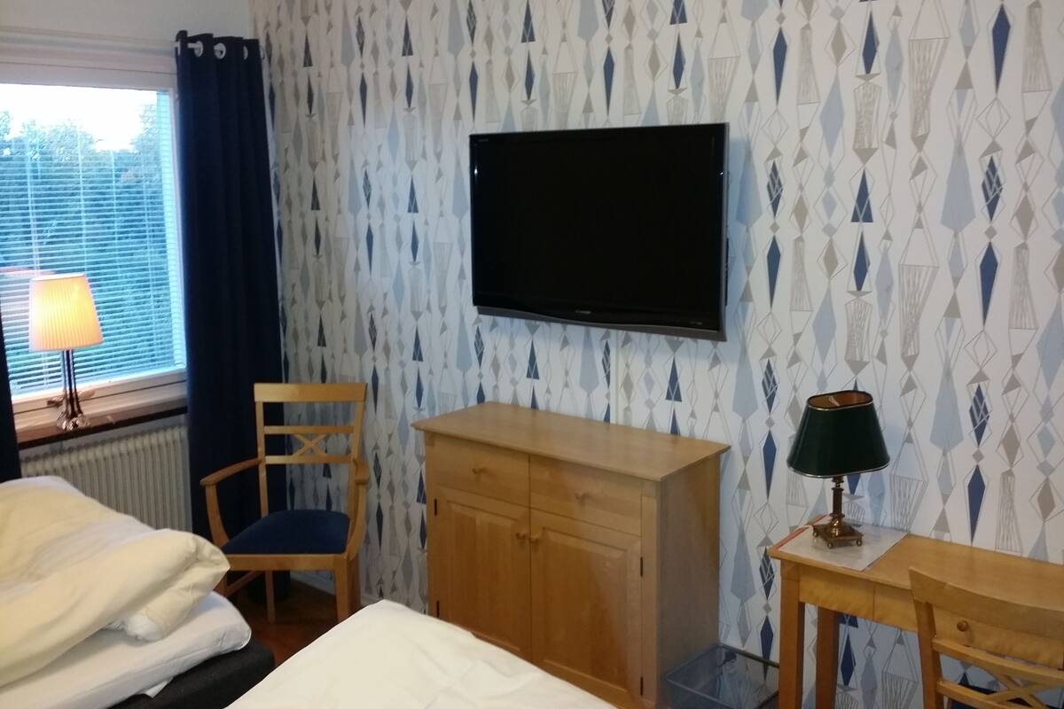 A hotel room with a bed, a desk, a chair, a TV, and a window with curtains.