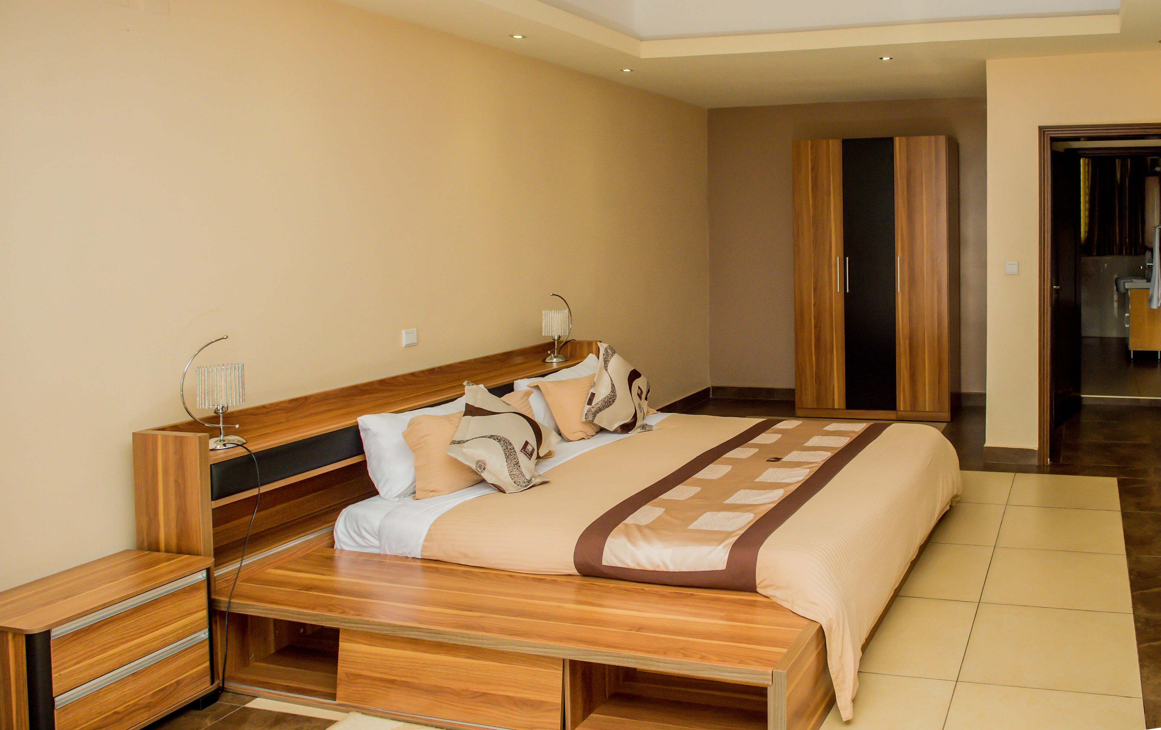 Een moderne slaapkamer met een houten bed, nachtkastjes, een garderobe en een zichtbare badkamer door een open deur.