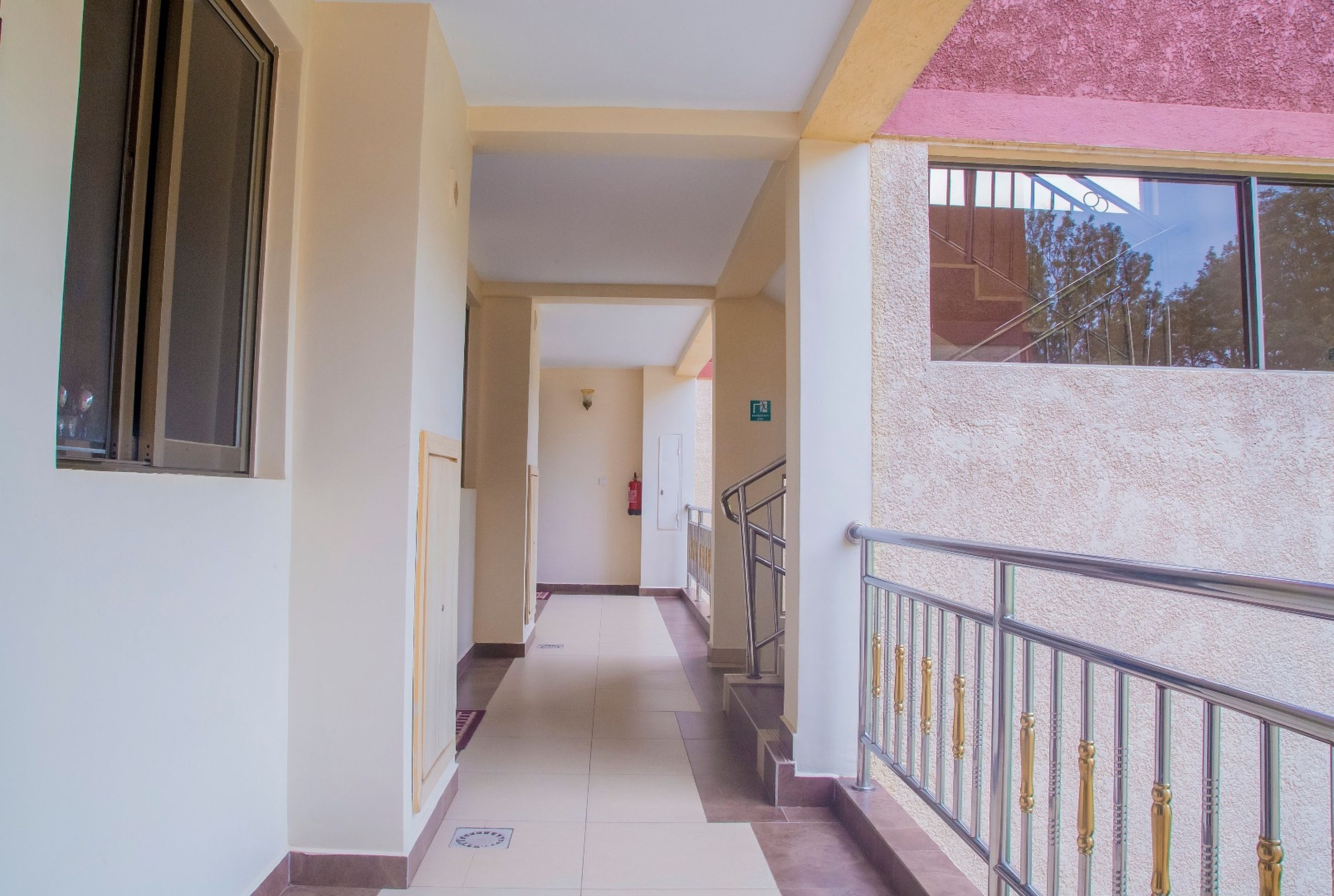 A corridor with a tiled floor, a metal railing on one side, and a door at the end.