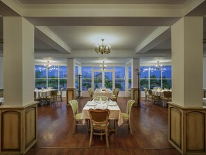 A dining area with tables set for service, large windows, and a chandelier.