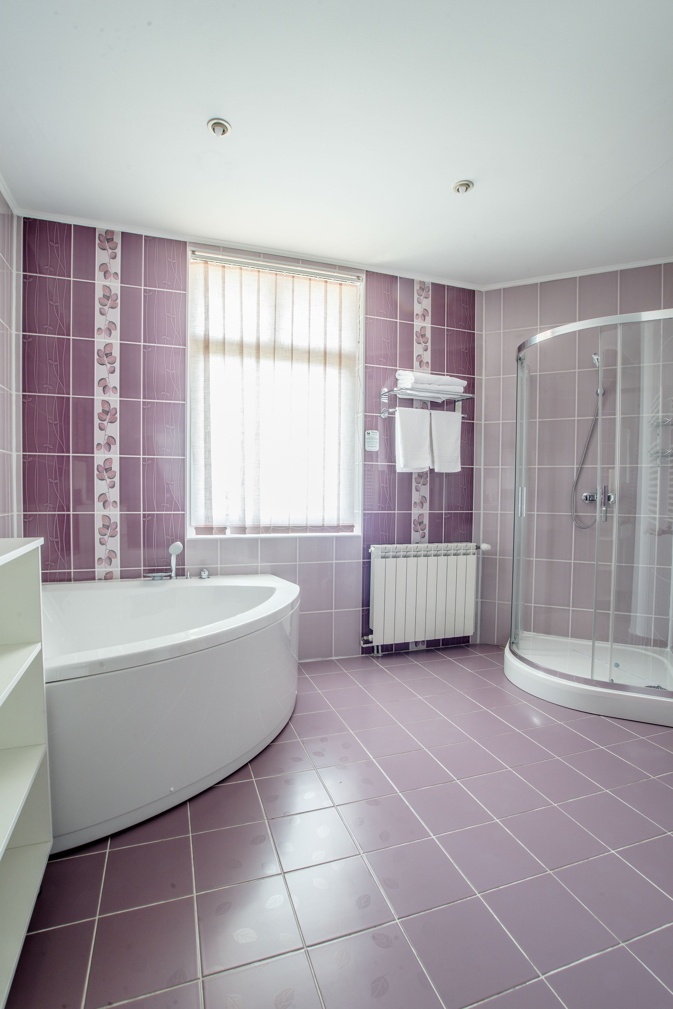 Un baño con bañera independiente, ducha con cerramiento de vidrio y ventana con persianas.
