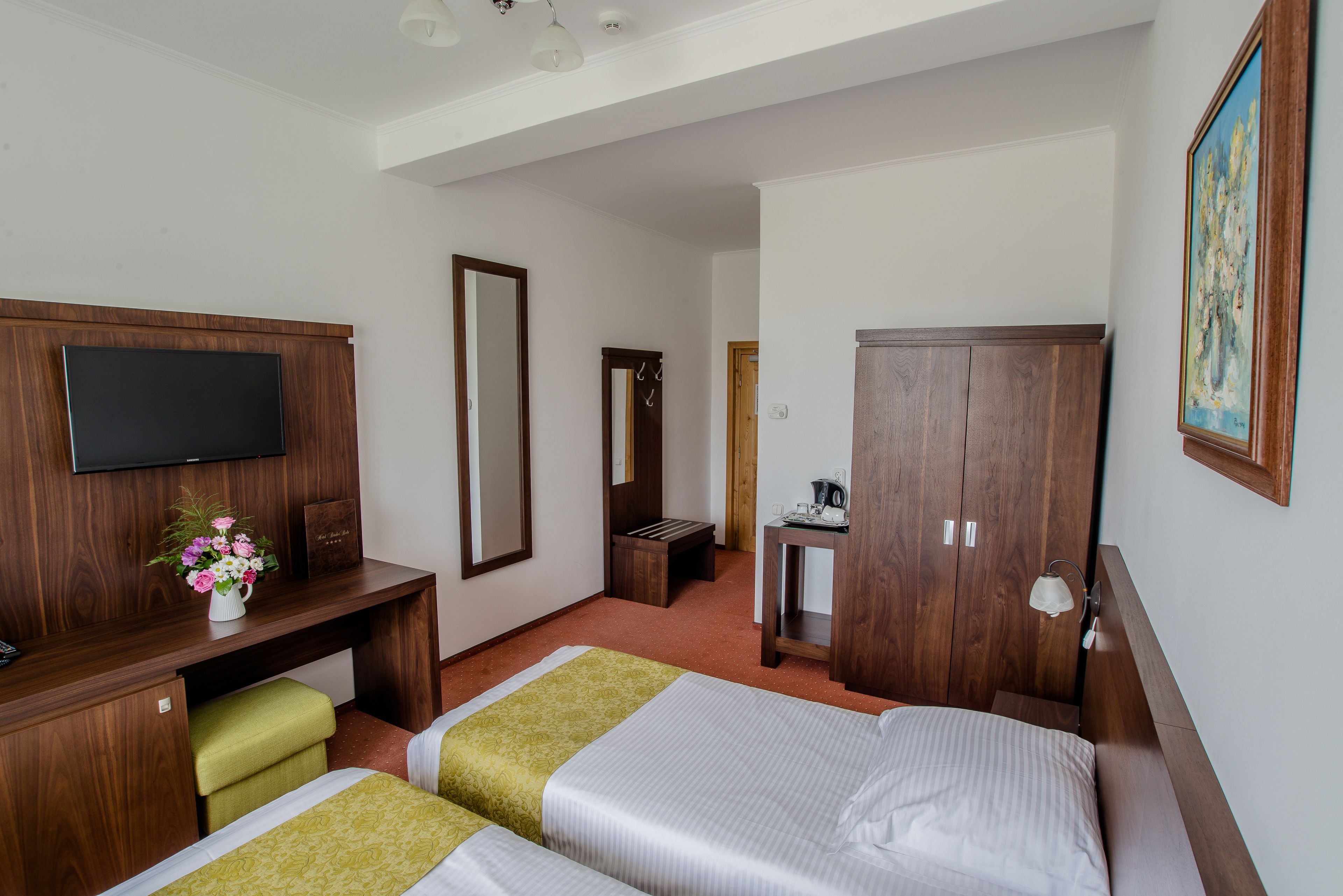 A hotel room with two beds, a desk with a TV, a mirror, and a wardrobe.